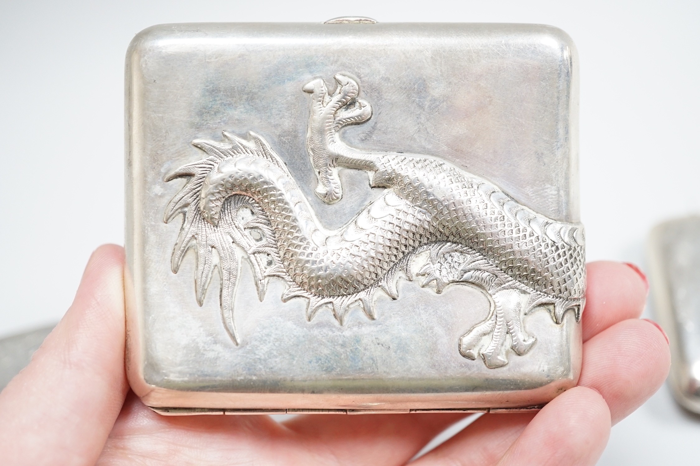 A white metal cigarette case, with applied dragon, 82mm, one other silver cigarette case and a Russian 84 zolotnik snuff box(tired).